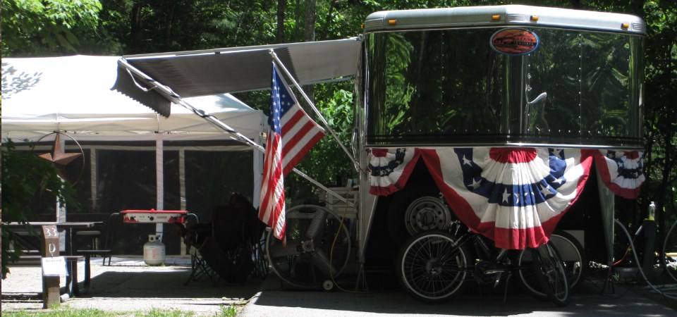 Patriotic flags hang from trailer parked in a camping spot.