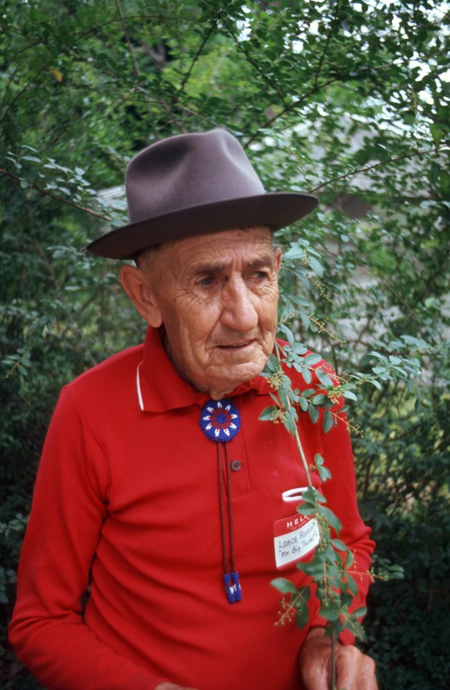 portrait of an old man wearing red long sleeve shirt, brown hat, and bolo tie