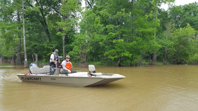 2 park rangers on a small boat on the river