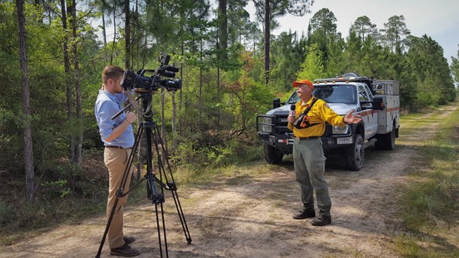 a firefighter talks to a news camera in front of a fire truck