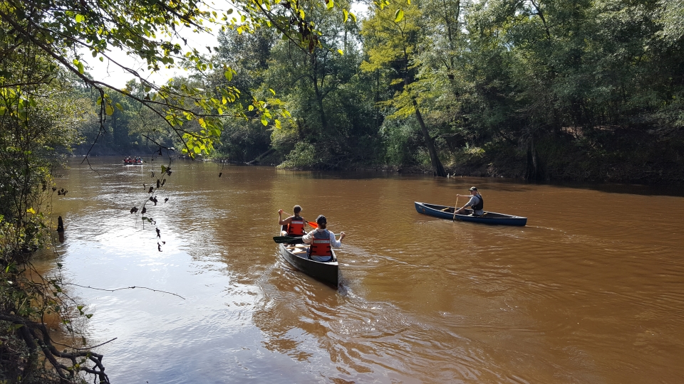 canoe trip one canoe with 2 people and another canoe with 1 person paddling down a wide river