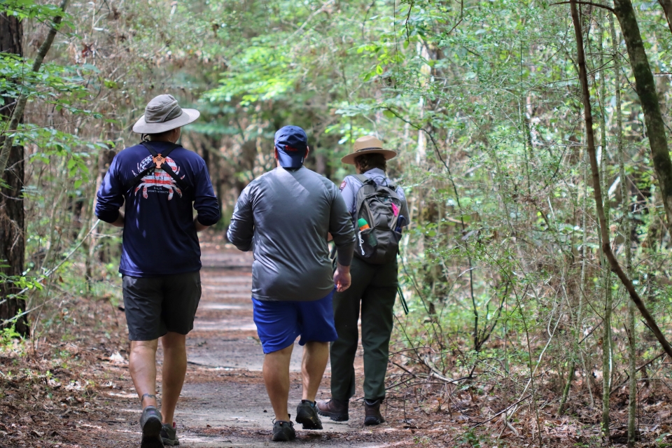 nature walk 2 people walking alongside a park ranger on a trail