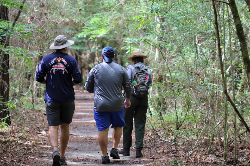 2 people walking alongside a park ranger on a trail