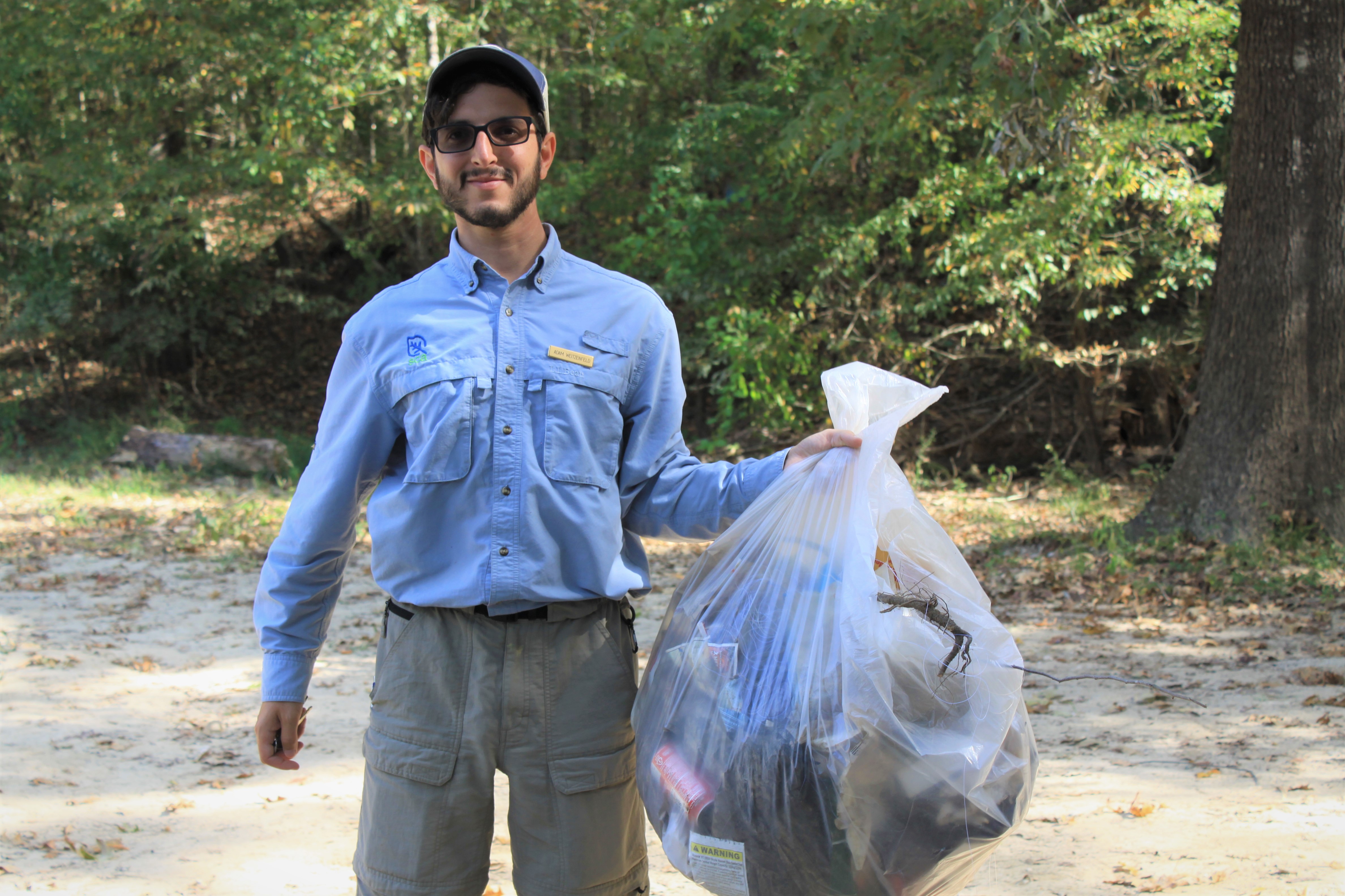 a person holding a full bag of trash in an outdoor setting