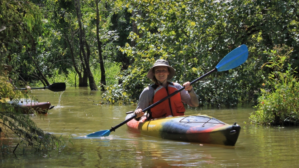 person paddling a multi-colored kayak on a narrow forested waterway