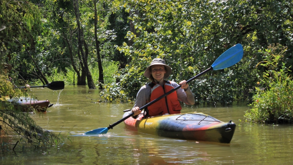 Kayakers person paddling a multi-colored kayak on a narrow forested waterway