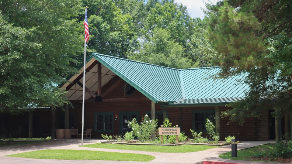 Big Thicket Visitor Center front of the big thicket visitor center, showing a flagpole, garden, lawn, and wooden sign that says "visitor center."