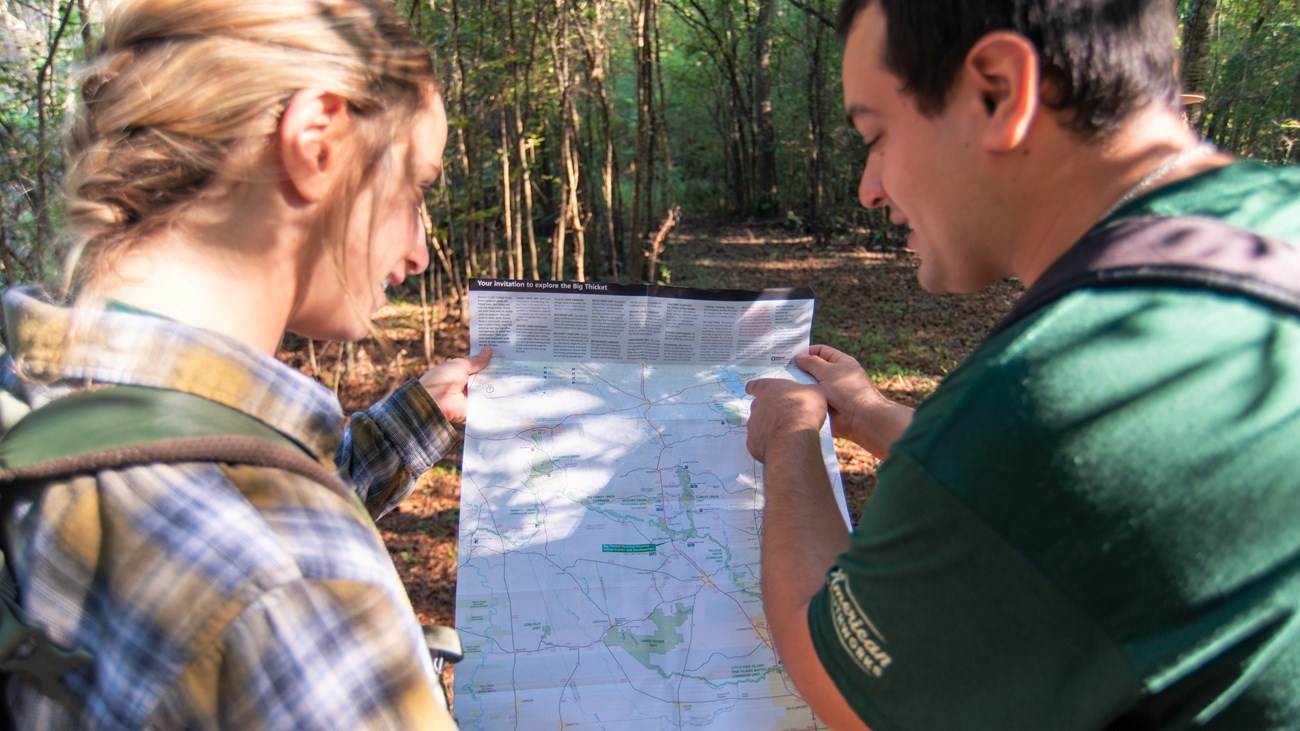 2 hikers looking a park map while on a trail in the woods.