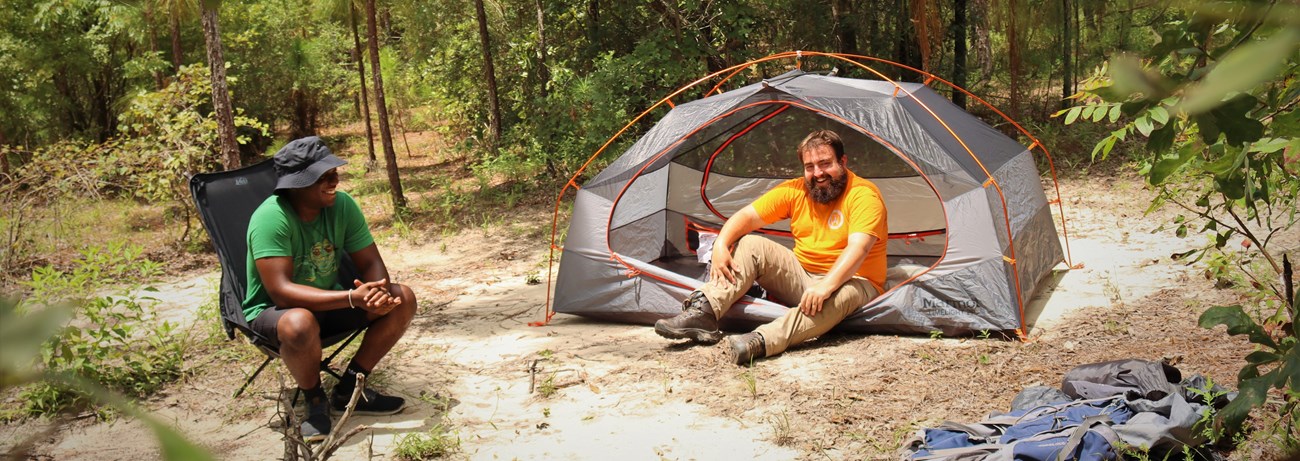 two people hanging out in a campsite in a sunny part of the forest