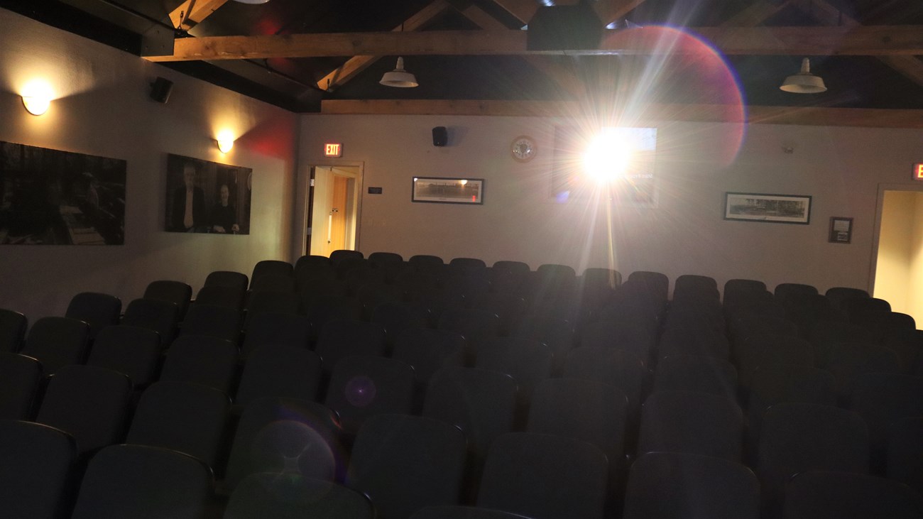 a small theater with many rows of chairs, with a bright lens flare coming from the projector.