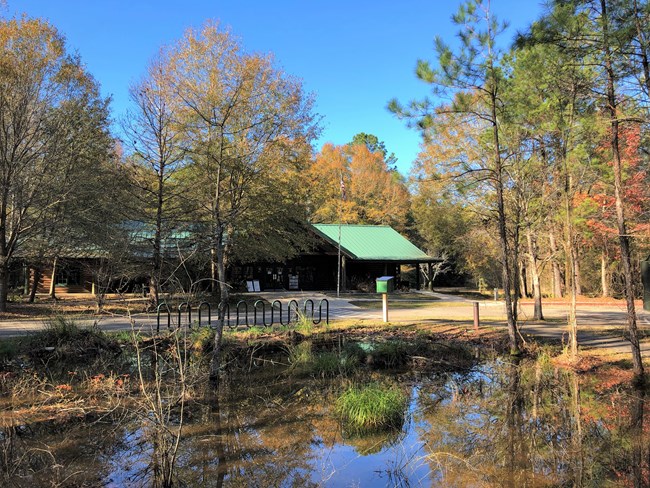 pond in front of wooden cabin structure surrounded by trees with fall colored leaves of red, yellows, and oranges.