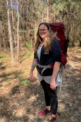 hiker wearing large backpack filled with camping gear, standing on a trail in the woods