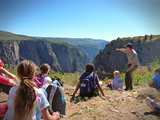A ranger points into a canyon while leading a program for young students.