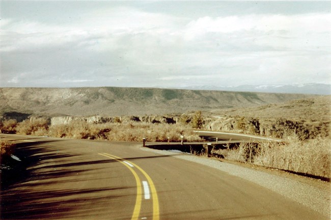 Sepia and red toned historic image of a completed, paved roadway along a canyon rim.