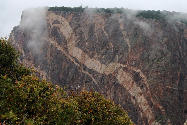 thick pink stripes of pegmatite in a large cliff face, fog