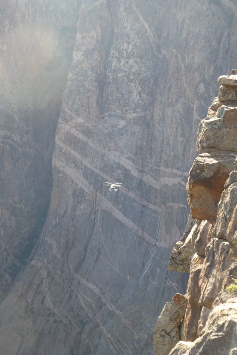 a helicopter, looking small against dark canyon walls hauls a line with rescuer and patient in litter.