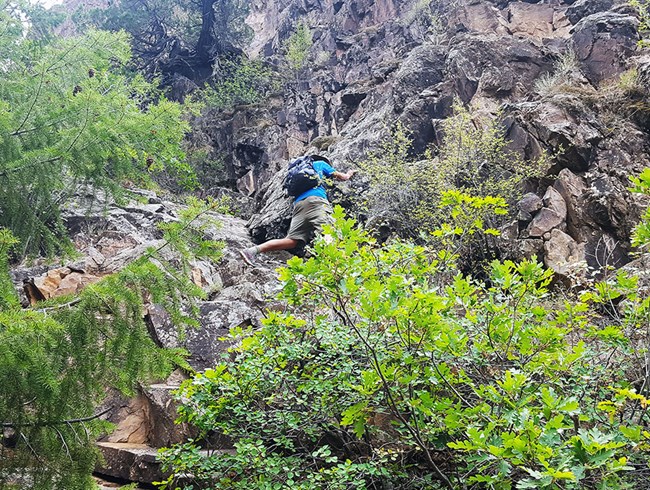 a male hiker clings to a sheer rock wall as he stands on a narrow ledge