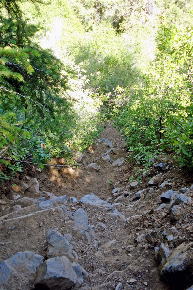 a thick metal chain descends as a hand hold along a steep, rocky path