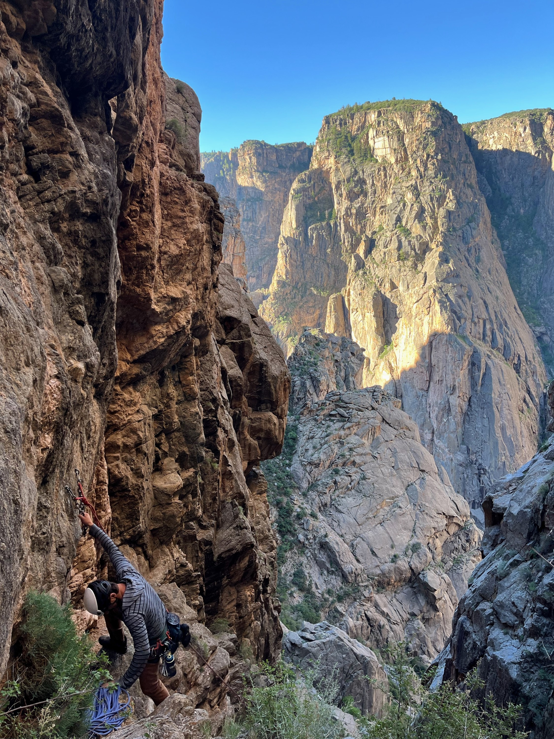 Climber in helmet and gear standing at the edge of Black Canyon's vertical cliffs showcasing the dramatic geological formations and canyon depth