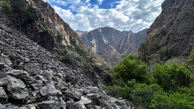 Red Rock Canyon approach with steep canyon walls, rock scree field, and blue sky with clouds above