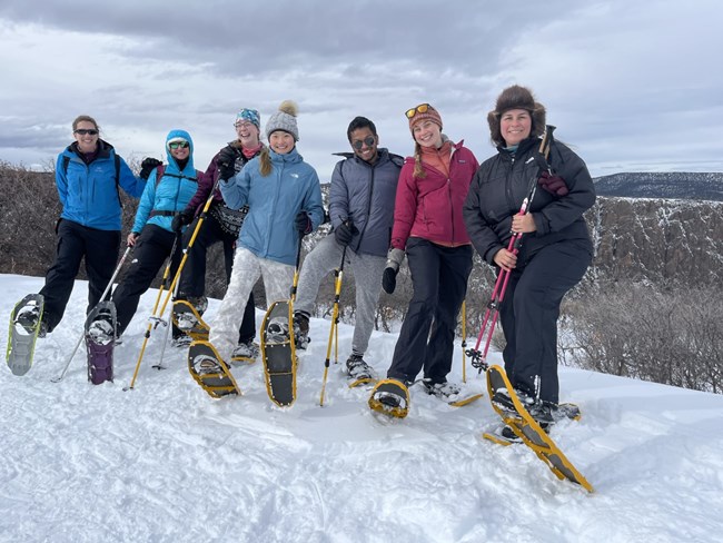 Seven snowshoers lift a shoe, canyon in background
