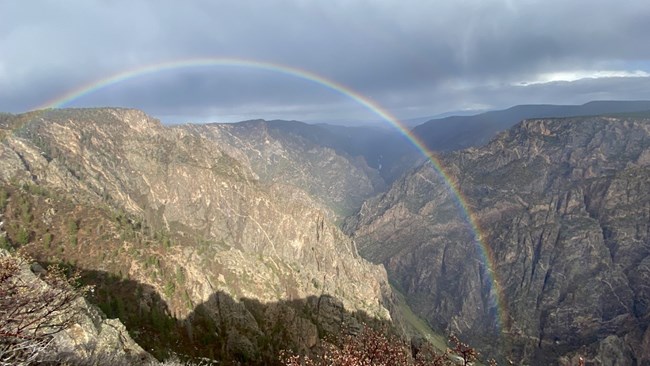 Rainbow arcs over canyon with storm clouds in background