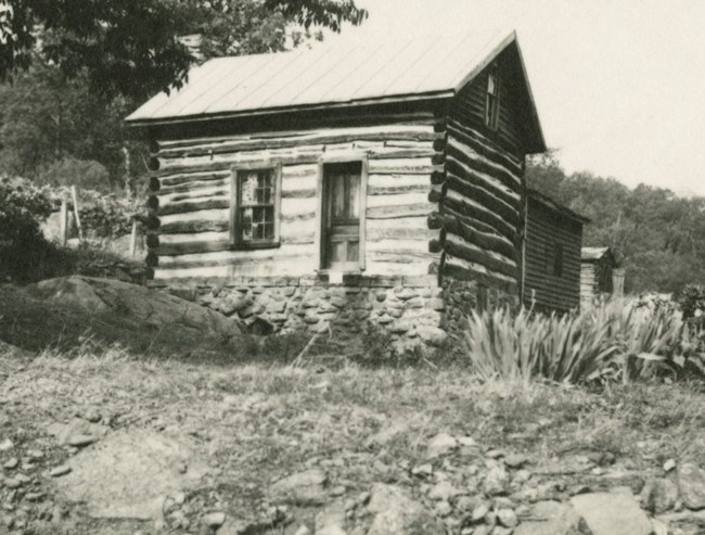 Photo of the main house at Saunders Farm circa 1950, with stone foundation, log siding, and metal roof.
