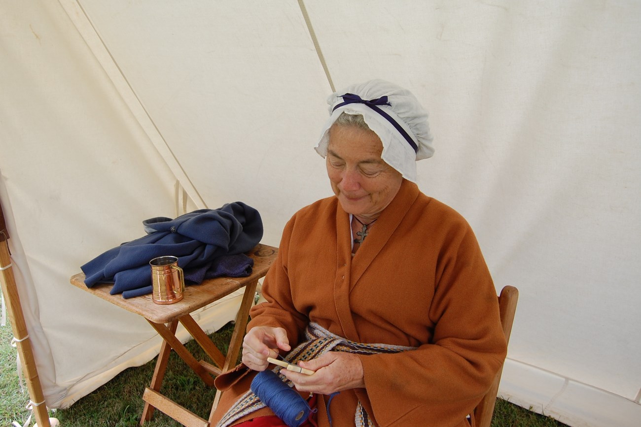 Woman in Revolutionary War Era attire working with her hands.