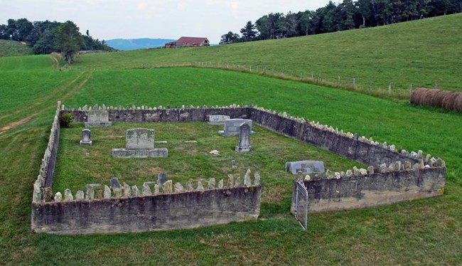 A small cemetery surrounded by a low, stone wall, sits in the middle of a grassy field