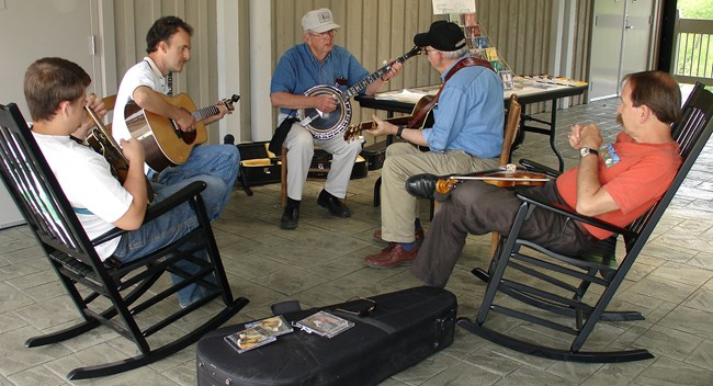 A group of 5 musicians playing guitars, banjo, mandolin and fiddle.