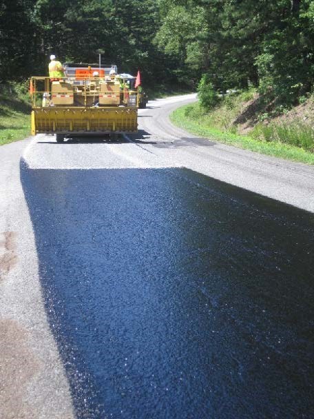 A construction vehicle spreads fine gravel on a treated road surface