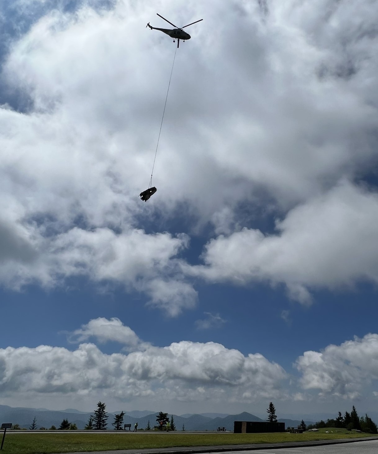 Airplane carrying portion of plane wreckage away from remote mountainside location.