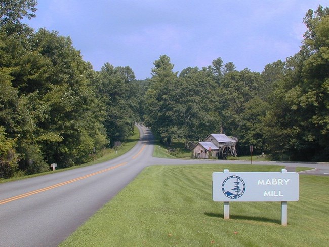 A sign next to the roadway that says "Mabry Mill" next to the Blue Ridge Parkway logo