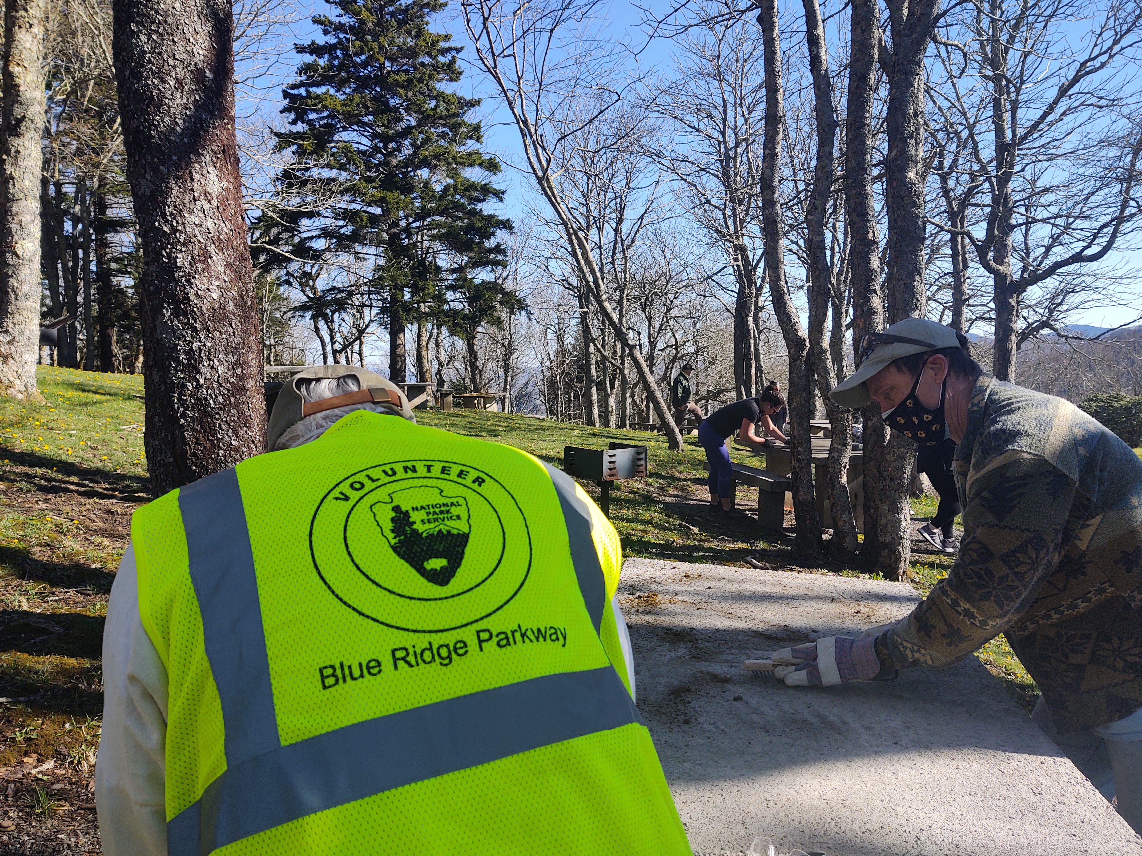 Two people clean an outdoor picnic table. Volunteers work in a picnic area.