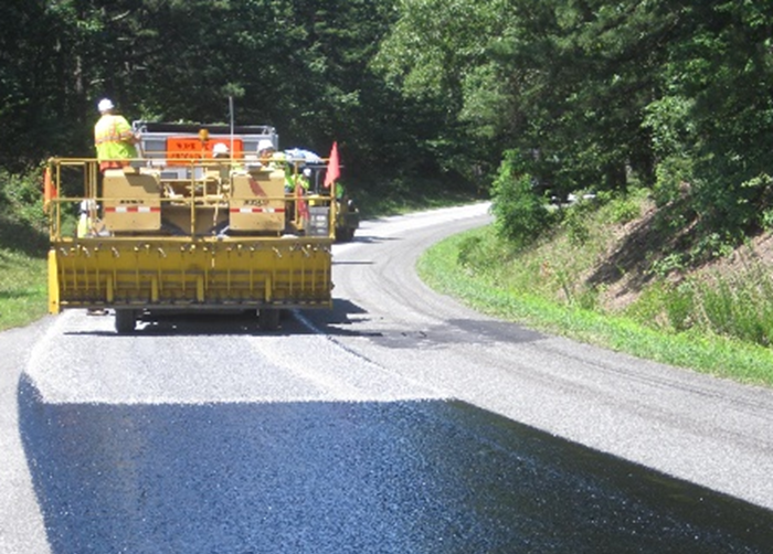pavement preservation A man on some machinery next to a freshly paved road.