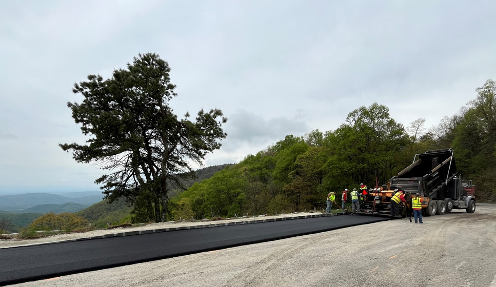 road construction news release A freshly paved road with workers in high-visibility vests to the side.