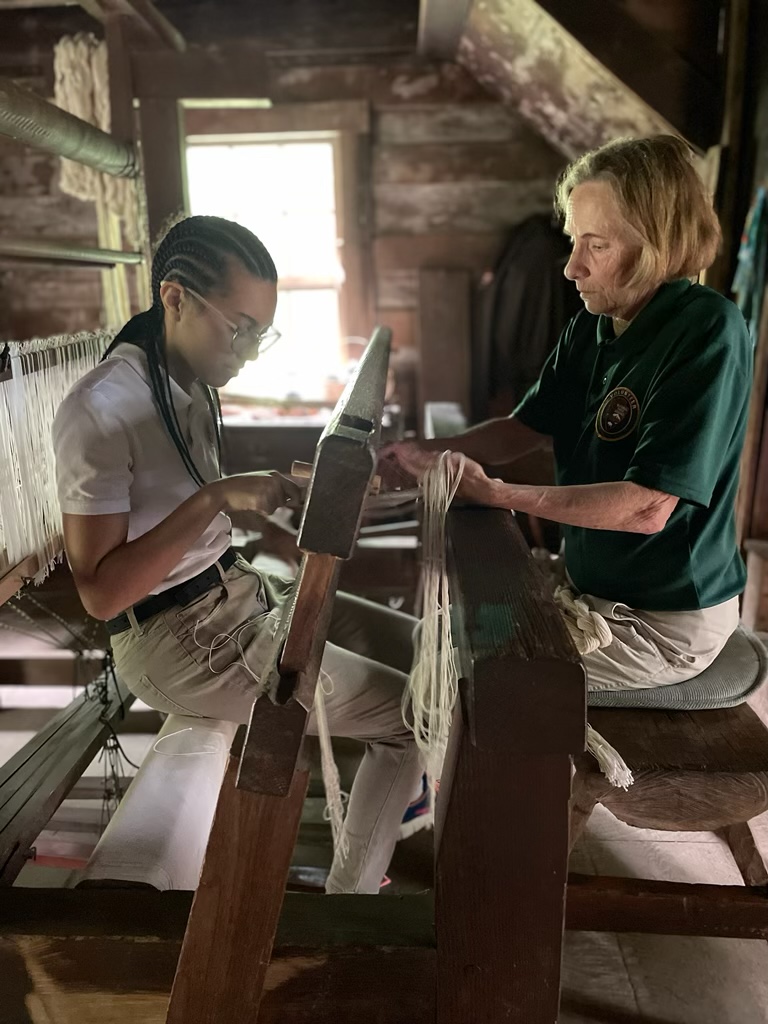 Youth volunteer at the loom weaving alongside adult volunteer.