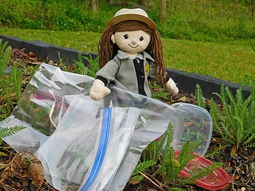A rag doll dressed like a female park ranger stands beside plastic bags