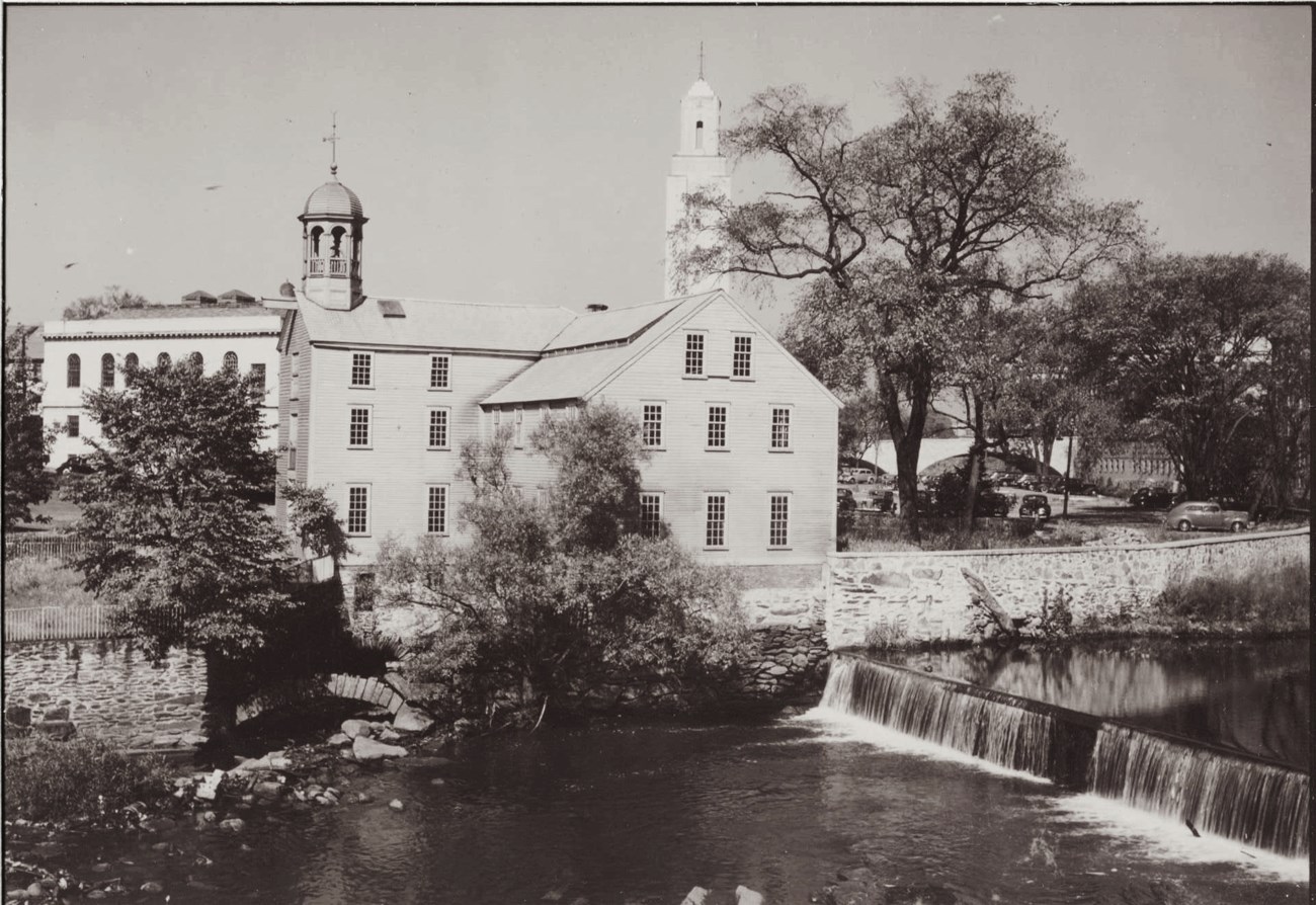 Black and white photograph of two story mill with tree in foreground