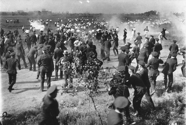 uniformed police run after running men. the police are holding weapons. there is smoke in the air.