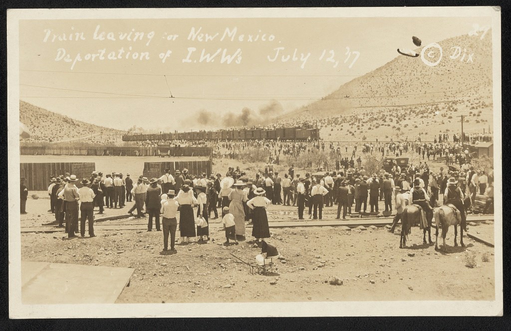 a group of men and women standing and watching and waiting for a train in the distance