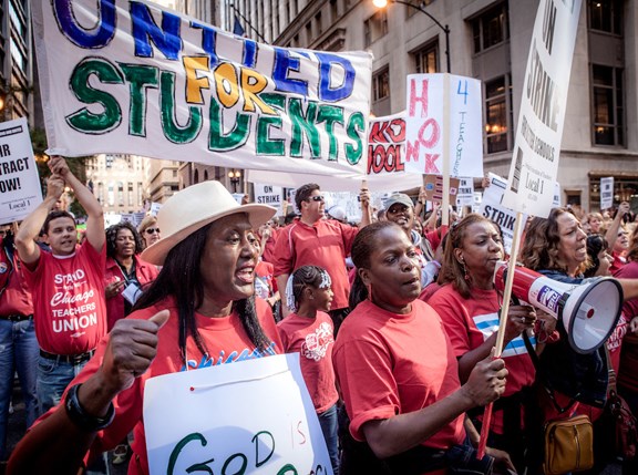 a group of people wearing red and holding picket signs and bullhorns