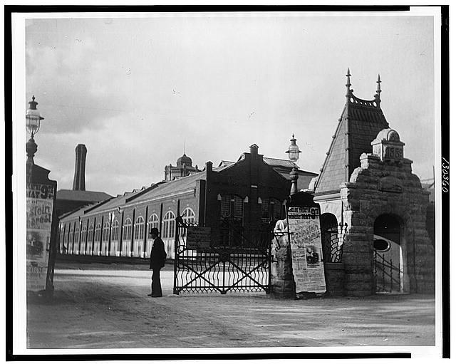 man standing outside large gate to a large factory complex