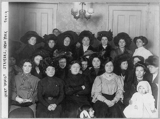 a group of women, with one man in the background and one child in the foreground, sitting for the camera