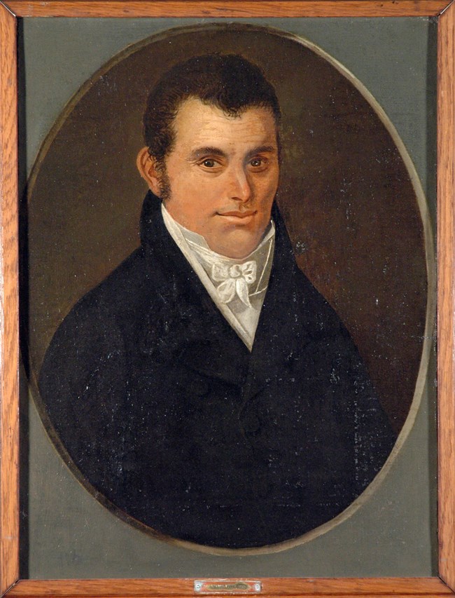 Portrait of a white male with black hair wearing a black suite with white shirt
