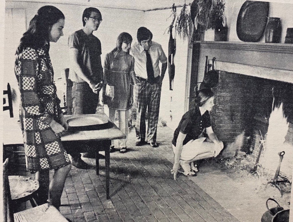 Black and white photo of visitors gathered around fire place in the Sylvanus Brown House