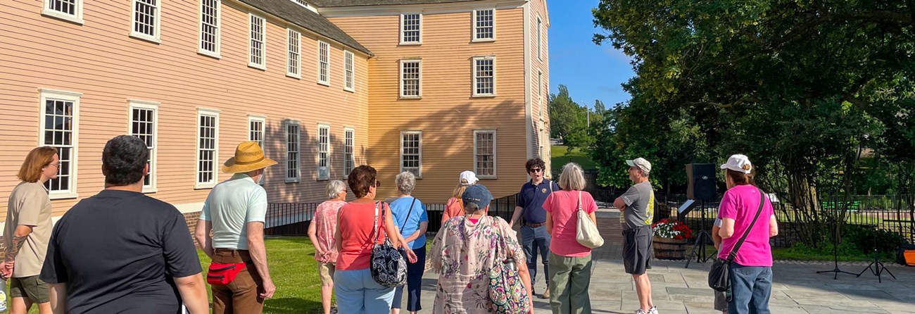 lt= An intern giving a tour in front of Slater Mill with visitors