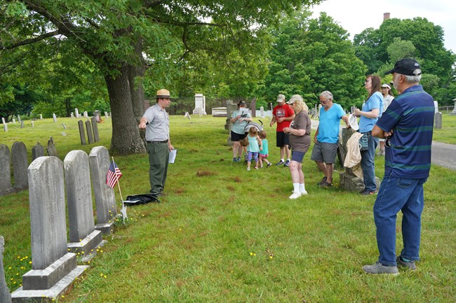 Cemetery Tour Park Ranger stands next to row of gravestones pointing while group of people listen