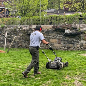 Park Ranger cutting grass on a push mower at Slater Mill