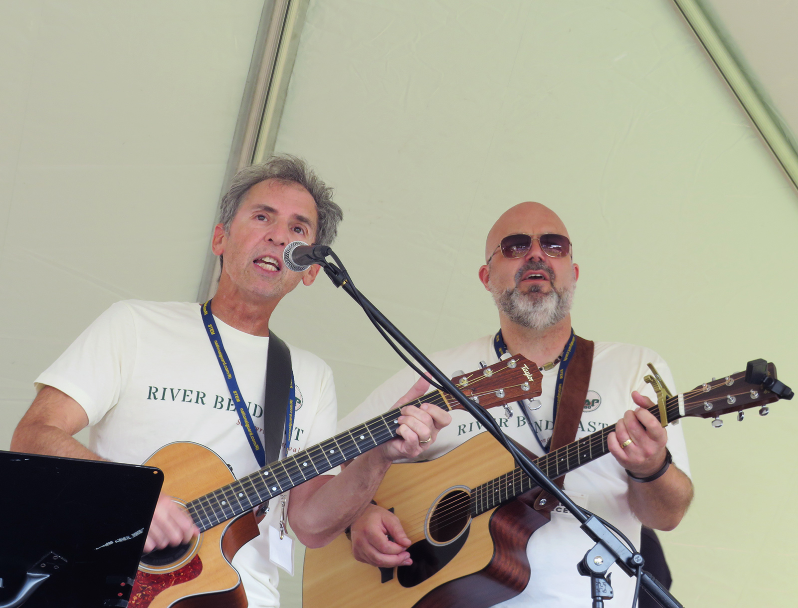 RB24_3 Two men singing while holding guitars under a tent